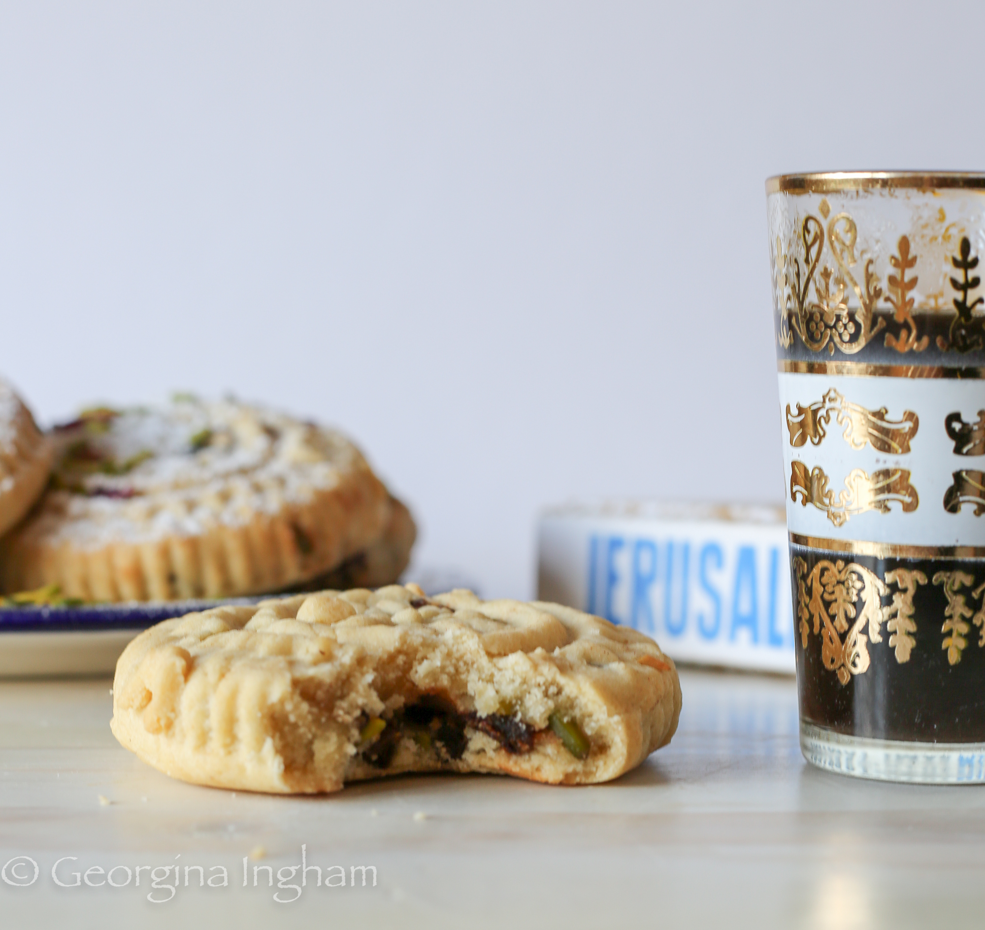Interior view of a ma&rsquo;amoul cookie on a wooden board, with the Jerusalem cookbook and Arabic coffee softly in the background.